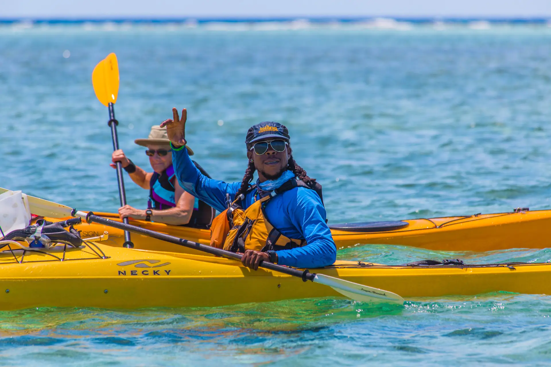 Guide waving in a kayak with his guests at Glover's Reef in Belize
